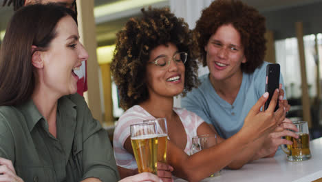 Grupo-Diverso-De-Amigos-Felices-Bebiendo-Cervezas-Y-Usando-Un-Teléfono-Inteligente-En-Un-Bar