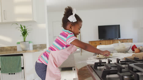 Happy-african-american-girl-rolling-dough-in-kitchen
