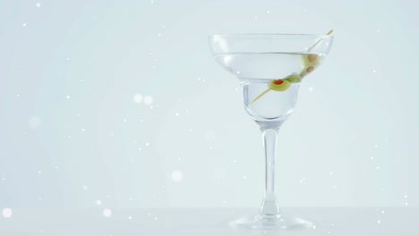 Weiße-Flecken-Schweben-über-Oliven,-Die-Vor-Grauem-Hintergrund-In-Ein-Cocktailglas-Fallen