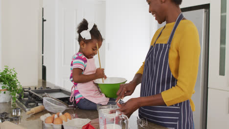 Happy-african-american-mother-and-daughter-wearing-aprons-cooking-in-kitchen