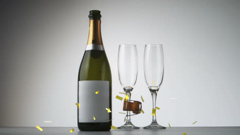 Animation-of-gold-confetti-and-cork-falling-over-champagne-bottle-and-glasses-on-grey-background