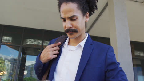 Mixed-race-man-with-moustache-walking-on-the-street-and-using-smartphone