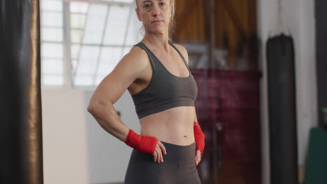Portrait-of-caucasian-female-boxer-with-hands-on-hips-standing-at-the-gym