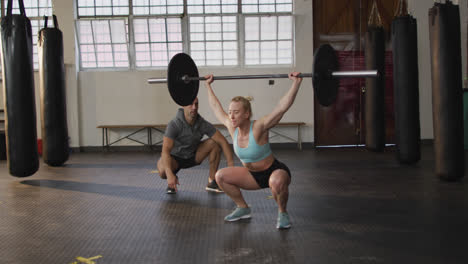Fit-caucasian-woman-working-out-with-barbell-with-male-trainer-at-the-gym