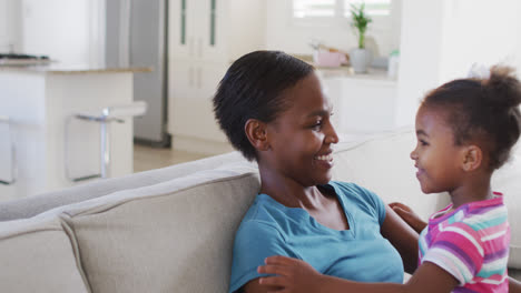 Happy-african-american-mother-and-daughter-sitting-on-sofa-and-hugging