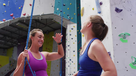 Two-caucasian-women-talking-and-high-fiving-at-indoor-climbing-wall