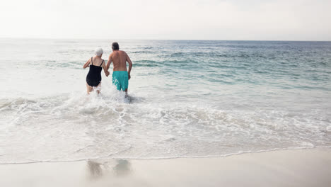 Caucasian-senior-couple-on-holiday-holding-hands-walking-in-sea