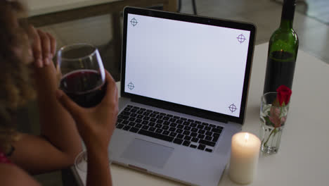 Mixed-race-woman-having-a-romantic-dinner-on-video-chat-using-laptop-with-copy-space