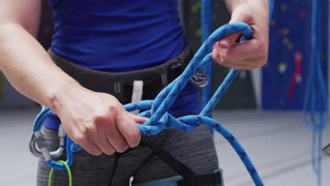 Midsection-of-caucasian-woman-securing-rope-in-a-harness-belt-at-indoor-climbing-wall