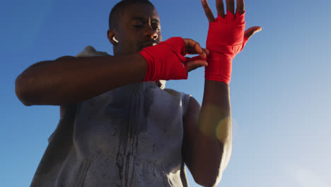 Focused-african-american-man-wrapping-his-hands,-exercising-outdoors