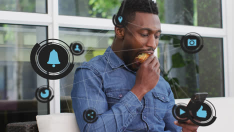 Network-of-digital-icons-moving-against-african-american-man-using-smartphone-while-having-a-snack