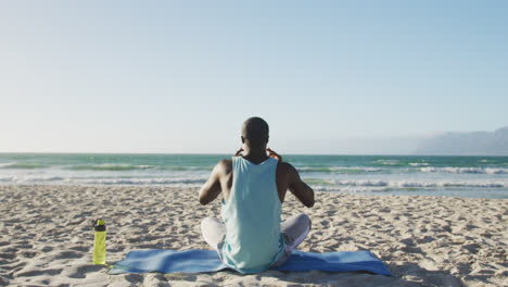 Hombre-Afroamericano-Practicando-Yoga-En-La-Playa,-Haciendo-Ejercicio-Al-Aire-Libre-Junto-Al-Mar