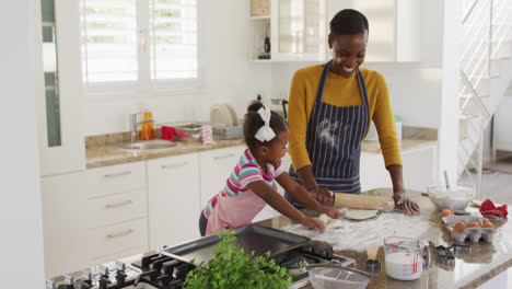 Happy-african-american-mother-and-daughter-wearing-aprons-having-fun-while-cooking-in-kitchen
