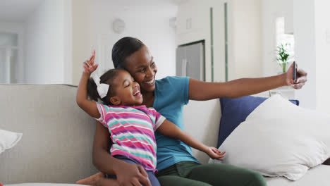 Feliz-Madre-E-Hija-Afroamericana-Sentadas-En-Un-Sofá-Tomando-Selfie-En-Casa