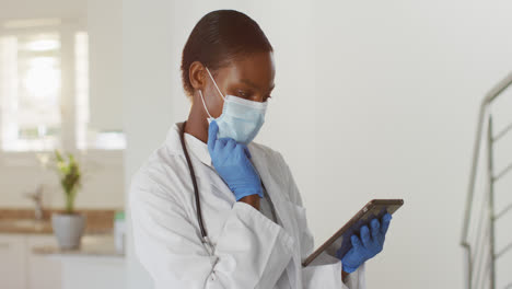African-american-female-doctor-wearing-mask-having-video-call-consultation-using-digital-tablet