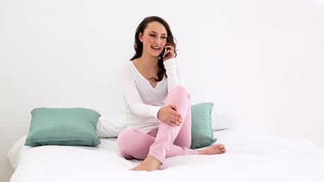 Smiling-woman-sitting-on-bed-talking-on-the-phone