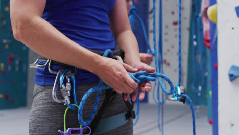 Midsection-of-caucasian-woman-knotting-rope-in-a-harness-belt-at-indoor-climbing-wall
