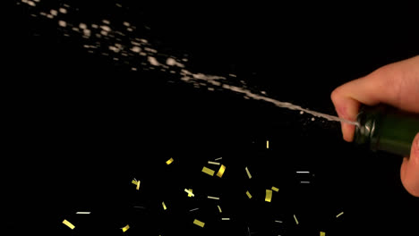 Golden-confetti-falling-over-mid-section-of-bartender-spraying-champagne-against-black-background