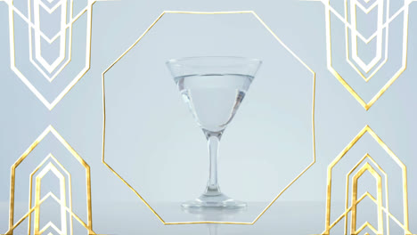 Goldener-Rahmen-Design-Muster-über-Oliven-Fallen-In-Cocktailglas-Vor-Grauem-Hintergrund