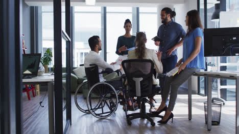Diverse-group-of-work-colleagues-talking-at-casual-office-meeting,-one-in-wheelchair