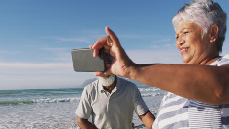 Lächelndes-älteres-Afroamerikanisches-Paar,-Das-Mit-Fahrrädern-Spazieren-Geht-Und-Ein-Selfie-Am-Strand-Macht