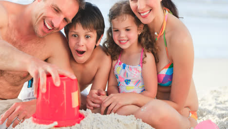 Portrait-of-smiling-caucasian-family-on-holiday-playing-with-sand-by-sea