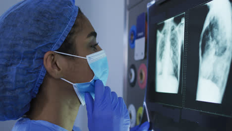 Mixed-race-female-surgeon-wearing-protective-clothing-looking-at-x-ray-on-screen