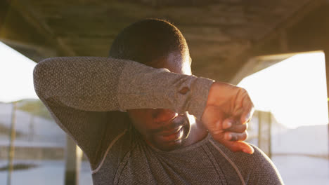 African-american-man-wiping-his-forehead,-taking-break-in-exercise-outdoors-in-the-evening