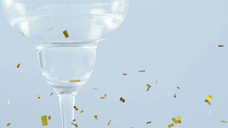 Golden-confetti-falling-over-olives-falling-into-cocktail-glass-against-grey-background