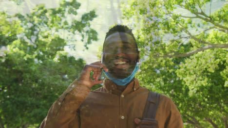 Waldweg-Gegen-Einen-Afroamerikanischen-Mann-Mit-Gesenkter-Gesichtsmaske,-Der-Beim-Gehen-Auf-Dem-Smartphone-Spricht