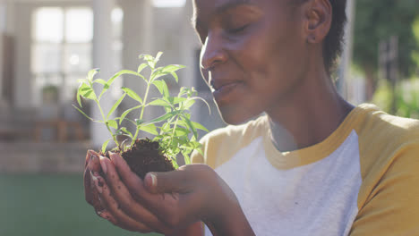 Feliz-Mujer-Afroamericana-Haciendo-Jardinería,-Sosteniendo-Y-Oliendo-Plantas-En-El-Jardín