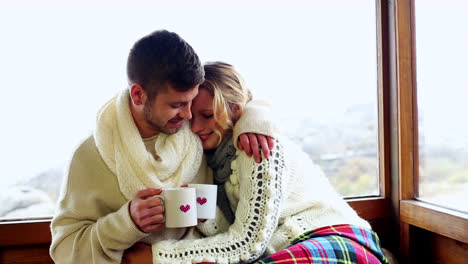 Cute-couple-cuddling-together-under-a-blanket-in-their-ski-lodge