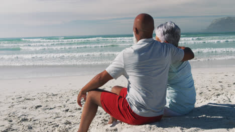 Senior-african-american-couple-sitting-and-embracing-at-the-beach