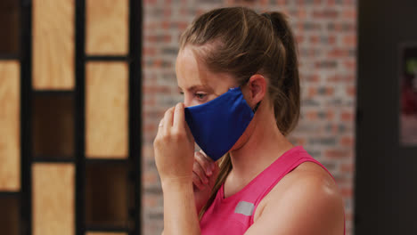 Portrait-of-caucasian-woman-at-a-sports-centre-adjusting-her-face-mask