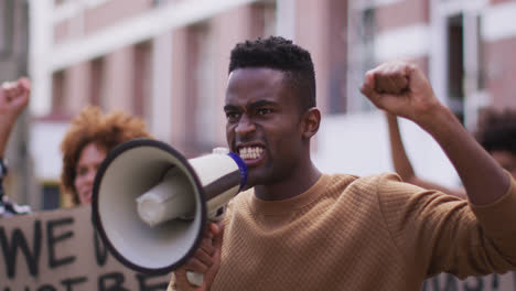 Hombre-Afroamericano-Gritando-Usando-Megáfono-Con-Otras-Personas-Sosteniendo-Pancartas-Durante-La-Protesta
