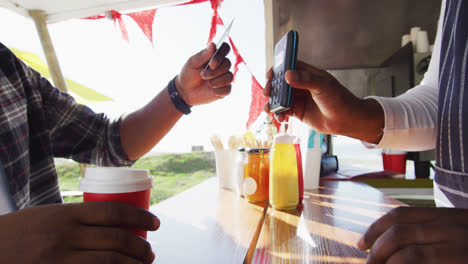 Midsection-of-african-american-man-paying-male-owner-for-coffee-by-credit-card-at-food-truck