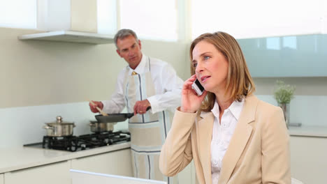 Businesswoman-talking-on-phone-while-husband-cooks-dinner