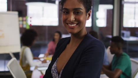 Happy-mixed-race-businesswoman-standing-and-smiling-with-colleagues-in-background