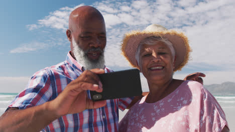 Una-Pareja-De-Ancianos-De-Raza-Mixta-Tomando-Un-Selfie-Con-Un-Teléfono-Inteligente-En-La-Playa