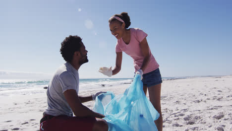 Afroamerikanisches-Paar-Gibt-Sich-Ein-High-Five,-Hält-Müllsäcke-In-Der-Hand-Und-Sammelt-Müll-Vom-Strand-Ein