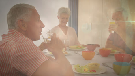 Animation-of-glowing-light-over-happy-senior-people-at-dinner-party