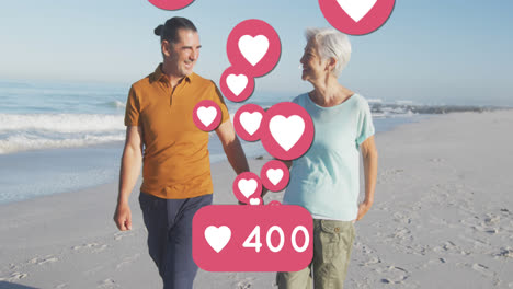 Animation-of-red-heart-love-digital-icons-and-numbers-over-smiling-senior-couple-on-beach