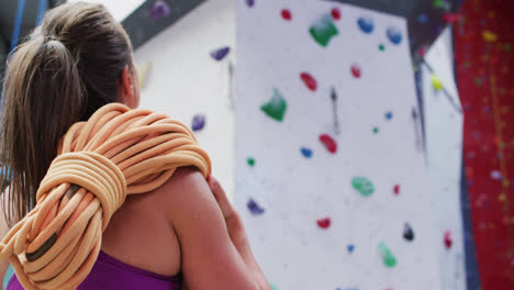 Rear-view-of-caucasian-woman-with-rope-over-her-shoulder-at-indoor-climbing-wall