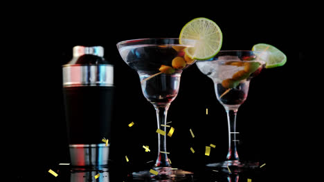 Golden-confetti-falling-over-ice-cubes-falling-into-cocktail-glasses-against-black-background