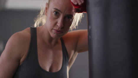 Portrait-of-caucasian-female-boxer-leaning-on-punching-bag-at-the-gym