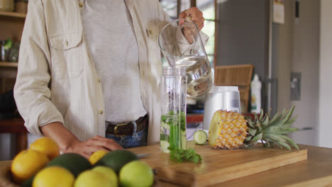 Midsection-of-mixed-race-woman-preparing-health-drink-standing-at-counter-in-cottage-kitchen
