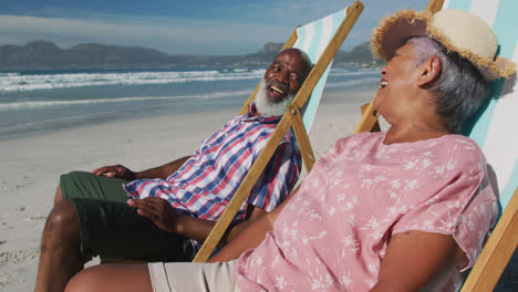 Älteres-Afroamerikanisches-Paar-Sitzt-Auf-Sonnenliegen-Und-Lächelt-Am-Strand