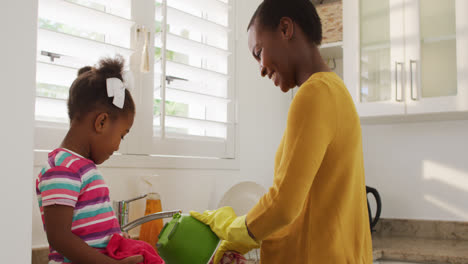 Happy-african-american-mother-and-daughter-washing-dishes-in-kitchen