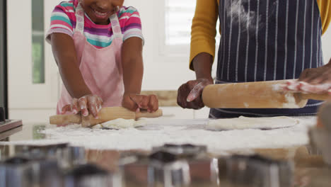 Happy-african-american-mother-and-daughter-rolling-dough-in-kitchen