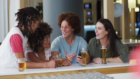 Diverse-group-of-happy-friends-drinking-beers-and-using-smartphone-at-a-bar